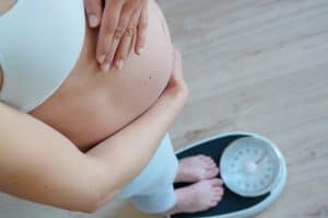 mulher grávida em cima de uma balança conferindo seu peso